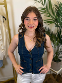 Woman wearing a denim vest and white pants in a room with plants and a rack.