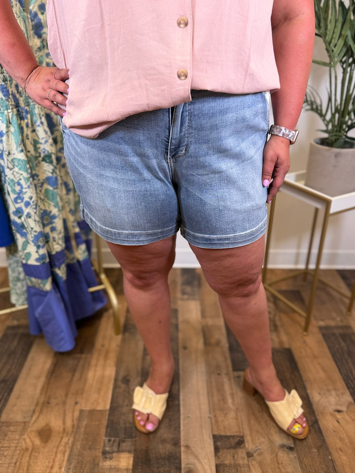 Person wearing a pink sleeveless top and light blue denim shorts on a wooden floor.