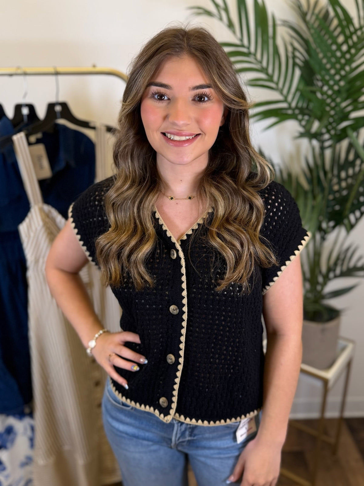 Woman wearing a black short sleeve crochet top with tan trim in a clothing store.