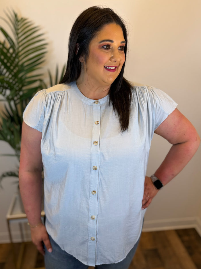 Woman wearing a light blue blouse with a plant in the background