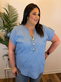Woman wearing a blue denim shirt with a plant in the background