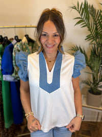 Woman wearing a white blouse with blue accents and ruffled cap sleeves in a clothing store.