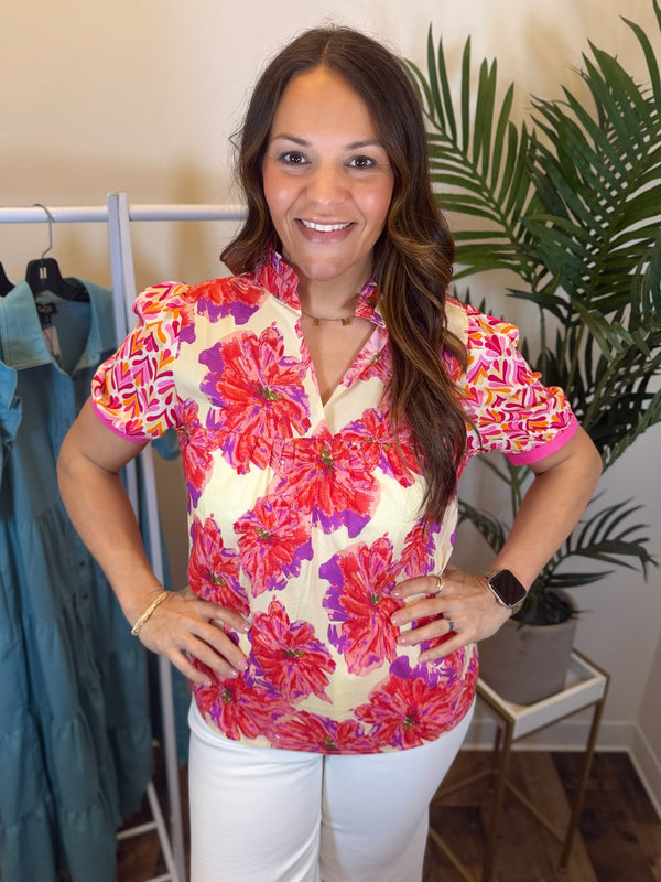 Woman wearing a colorful floral blouse with short sleeves and split neckline in a clothing store.