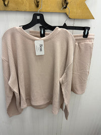 A ribbed knit two-piece loungewear set in a light taupe color, featuring a long-sleeve top and matching shorts, hanging on black hangers against a white paneled wall.